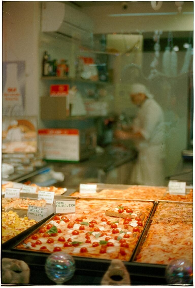 Delicious variety of freshly baked pizzas on display in a local bakery with a chef in the background.
